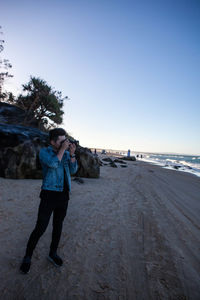 Full length of young man standing at beach against clear sky
