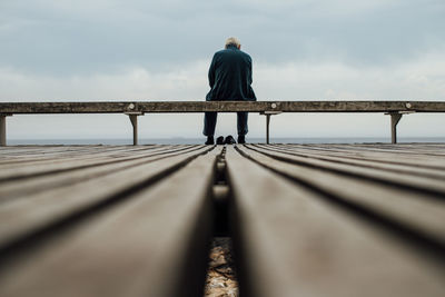 Rear view of man sitting at beach against sky