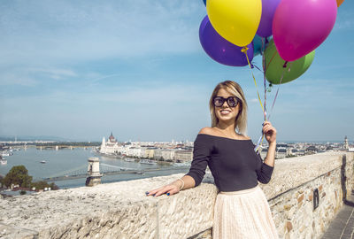 Woman with colorful balloons on walkway against sky in city