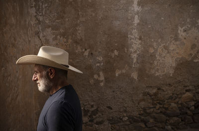 Side view of adult man in cowboy hat against wall
