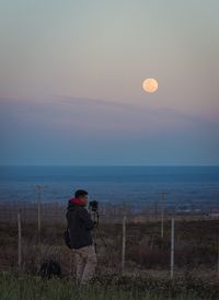 Man photographing sea against sky during sunset