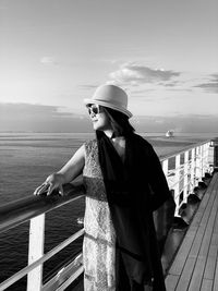 Woman wearing sunglasses while standing by railing of boat in sea against sky