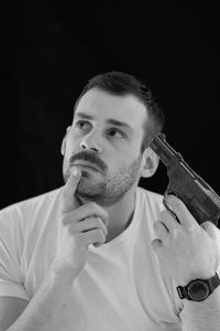 Thoughtful man attempting suicide with gun against black background