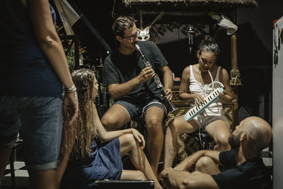 Man and woman playing musical instruments while sitting with friends at tourist resort