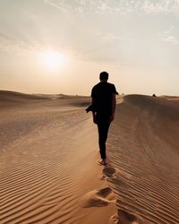 Rear view of man on beach against sky during sunset