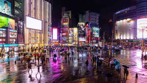 People by illuminated buildings in city at night