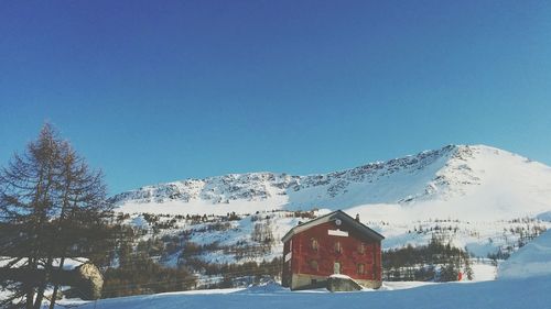 House by snowcapped mountain against clear sky