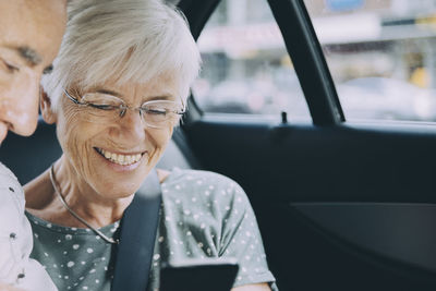 Smiling senior woman showing mobile phone to man while sitting in car