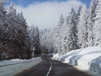 Snow covered road amidst trees against sky