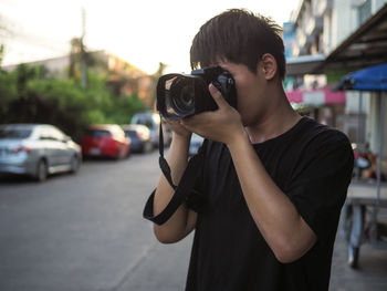 Teenage boy photographing with camera while standing on road against sky