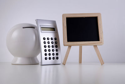 Close-up of piggy bank and calculator with blackboard on table against white background