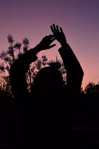 Silhouette woman with arms raised against sky during sunset