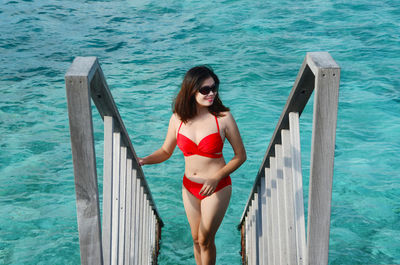 Portrait of beautiful woman standing on railing against sea