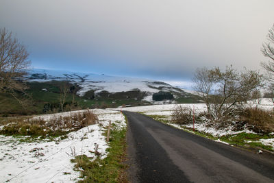 Empty road by snowcapped mountains against sky during winter