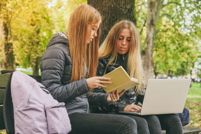 Girls study sitting on a bench in the park. students teens using laptop and reading a book outdoor. 