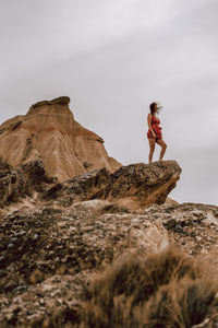 Side view of woman on rock against sky