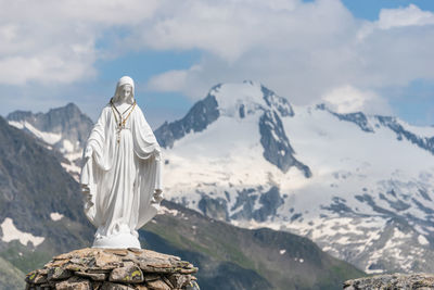 White statue of virgin mary, mother of god, placed on top of the mountain, blue sky, white clouds.