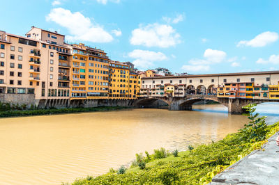 Arch bridge over river by buildings against sky