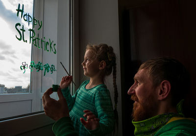 Girl writing on window with father at home