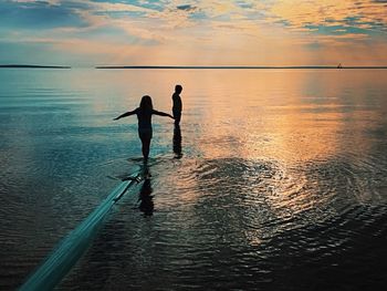 Silhouette people standing on sea against sky during sunset