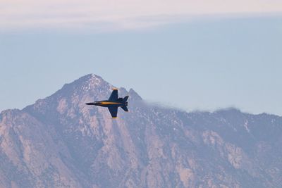 Low angle view of airplane flying in mountains against sky