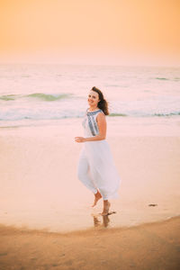 Full length of woman standing at beach against sky during sunset