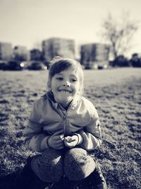 Smiling cute girl looking away while crouching on grass against sky