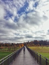 Rear view of man walking on railing against sky