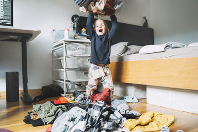Carefree boy throwing laundry clothes in bedroom at home