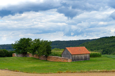 House on field by trees against sky