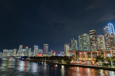 Illuminated buildings by river against sky at night