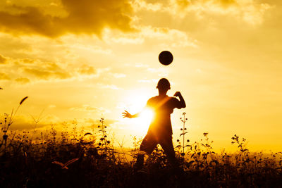 Silhouette boy playing soccer on field against sky during sunset