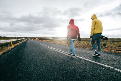 Full length of young man and woman skateboarding on road against landscape