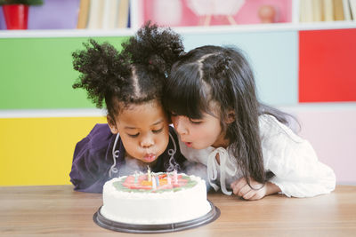 Girls blowing candles on birthday cake at preschool classroom