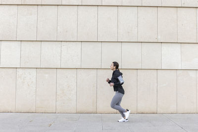 Active woman jogging on footpath by wall