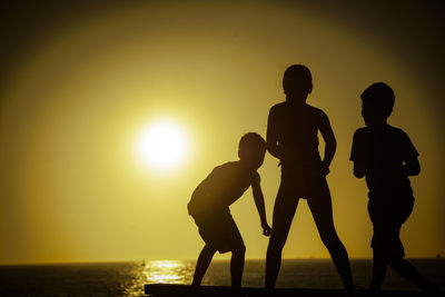 Rear view of silhouette siblings in front of sea at sunset