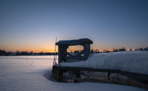 Lifeguard hut on snow covered landscape against sky during sunset