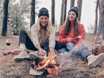 Smiling women burning campfire in forest