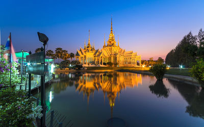 Illuminated building by lake against blue sky at dusk