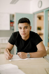 Portrait of teenage boy studying while sitting by table in classroom