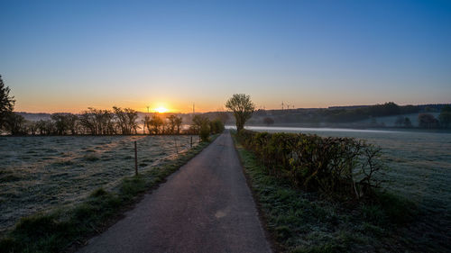 Road by river against sky during sunset