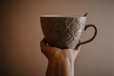 Close-up of hand holding coffee cup against wall