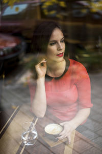 Beautiful young woman having coffee seen through glass window