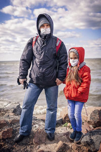 Father and daughter wearing respirator masks staying together on the empty bank of sea