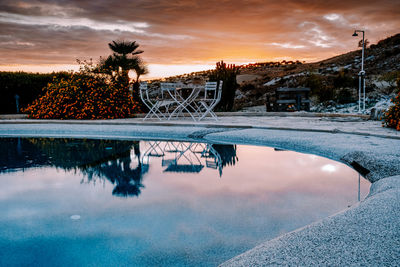 Reflection of trees in swimming pool against sky during sunset