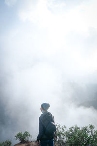 Rear view of man standing against cloudy sky