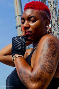 Low angle portrait of young woman with finger on lips standing by fence