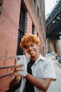 Man smiling in vintage clothing on street with mobile phone for selfie