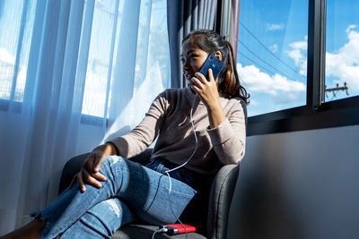 Full length of woman sitting on window