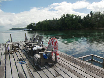 Empty chairs and tables by pier on island pier  against sky